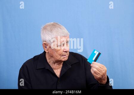 A senior old man with grey hair, sun damaged skin and a hearing aid looking puzzled at his credit card or cash card perhaps wondering why it doesn't w Stock Photo