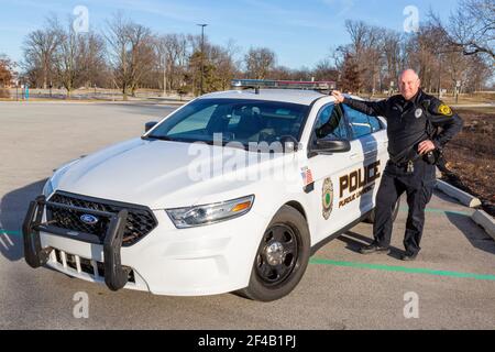 A Purdue University Fort Wayne police officer stands next to a white patrol car on campus. Stock Photo