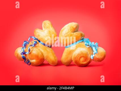 Two Easter bread bunnies facing each other on red background. Cute rabbit shaped yeast bread buns with ribbons. Swiss butter bread called Zopf. Concep Stock Photo