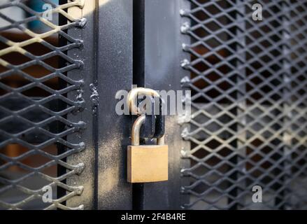 Padlock on outdoor door, close up. Caged in commercial or residential area. Golden metal lock on black fence with reinforced mesh and gold spray paint Stock Photo
