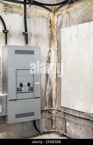 Active water leak stain on concrete wall in building service room. Electrical cabinets with splatters. Rough water damage stain with wet, brown and ef Stock Photo