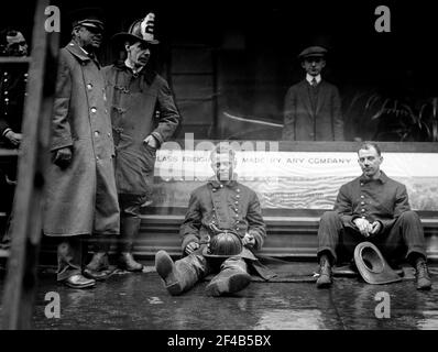 Firemen seated on the sidewalk after fighting a fire in a New York City subway tunnel which took place near West 55th Street and Broadway, January 6, 1915