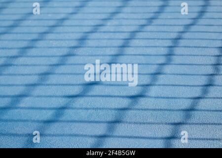 Abstract tennis court texture. Defocused tennis net shadow on ground, outside early morning. Blue rubberized and granulated ground surface for shock a Stock Photo