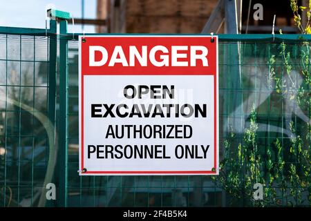 Construction site safety signage with text: Danger, open excavation, authorized personnel only. Large sign or poster on green construction fence. Stock Photo