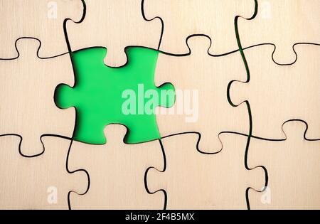 Missing puzzle piece. Almost finished, large jigsaw puzzle made of wood on green background. Concept for moving forward, understand a process. Stock Photo