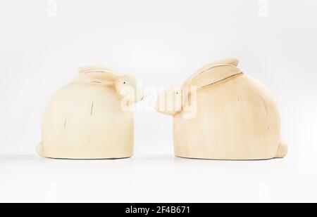 Facing wood rabbits. Two adorable simple bunnies facing each other. Off white or yellow color with soft white background. Easter themed table decorati Stock Photo