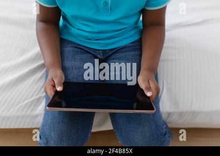 Midsection of african american boy sitting on couch using digital tablet Stock Photo