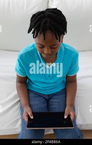 High angle view of african american boy with short dreadlocks sitting on couch using digital tablet Stock Photo