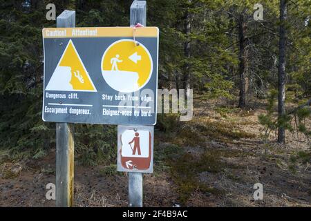 Sign Post Warning Hikers to Stay off Eroded Cliffs on Siffleur Falls Hiking Trail in Canadian Rockies with Green Forest in Background Stock Photo