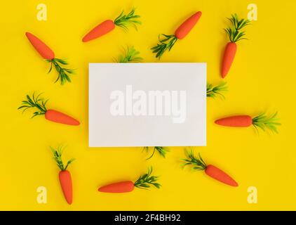 Blank paper card with carrots on a yellow background. Easter composition. Spring holidays concept. Stock Photo