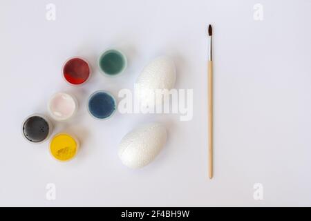 White clean decorative eggs, paints and brushes on white background top view, flat lay. Easter symbols. painting eggs. Creativity with children for de Stock Photo