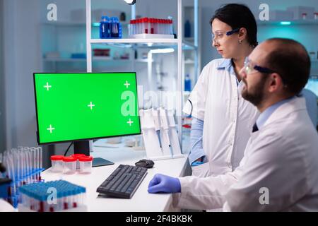 Modern medical research laboratory with two scientists using computer with green chroma key screen. Doctors specialists discussing innovative treatment against covid19 using high technology equipment Stock Photo