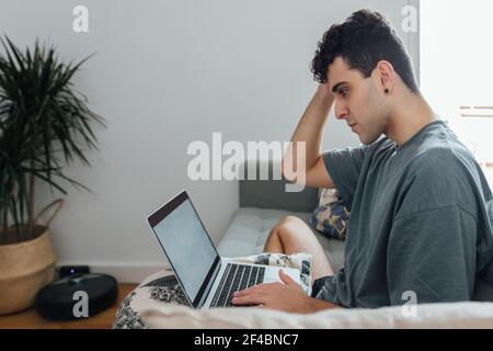 A young Caucasian male using his laptop while sitting on the sofa Stock Photo