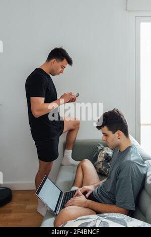 A young Caucasian gay couple using a laptop and smartphone in the living room Stock Photo