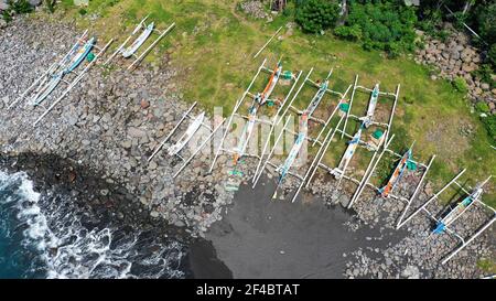 Top down aerial of traditional jukung boats resting on beach in Bali. Amed beach in Bali Indonesia with Jukung fishing boats lined up on the shore Stock Photo