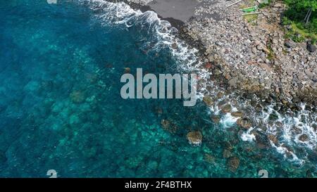 Aerial top view waves break on dark rocks near beach. Sea waves on the dangerous stones aerial view drone 4k shot. Bird's eye view of ocean waves Stock Photo