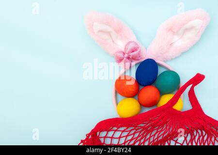 Easter shopping concept. Hand painted Easter eggs, pink bunny ears and a red shopping bag on a blue background, copy space, top view, flat lay. Happy Stock Photo
