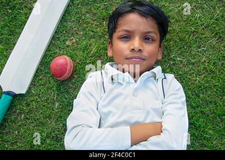 top angle view young boy lying on the ground with cricket ball and cricket ball Stock Photo