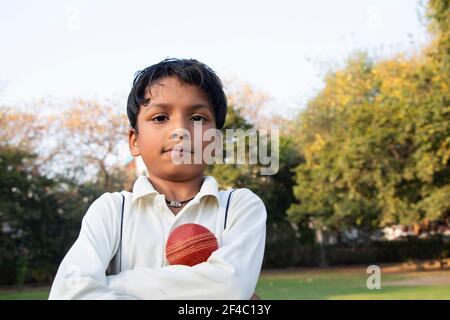 A boy in cricket uniform standing with cricket ball Stock Photo