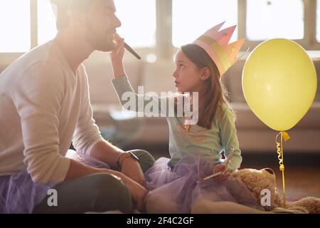 A little ballerina who puts makeup on her father's face while they are preparing for a training in a relaxed atmosphere at home. Family, ballet, train Stock Photo