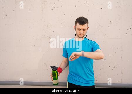 Man looks at smart watch, check the number of calories, heart rate, training time, in his hand a with a bottle of water, in summer in the city Stock Photo