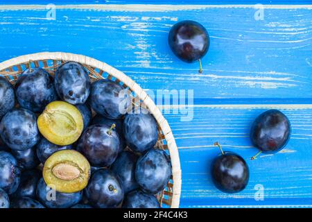 Ripe plums in bowl on blue wooden table, directly above. Fresh harvested plum fruit Stock Photo