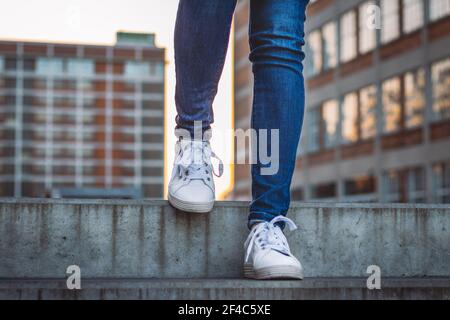 Woman wearing jeans and white sneakers is walking on stairs. Stylish hipster in city, close-up front view to legs Stock Photo
