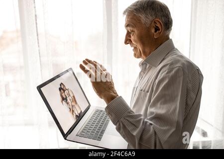 Handsome old man dressed in casual formal style using laptop, while sitting on sofa at home. Happy grandfather communicate with grandchildren. Video Stock Photo