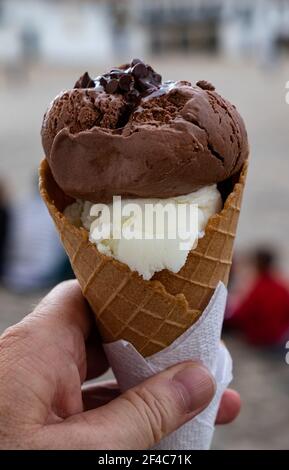 Chocolate and vanilla ice cream scoops, topped with chocolate chips, sit atop a waffle cone. Stock Photo