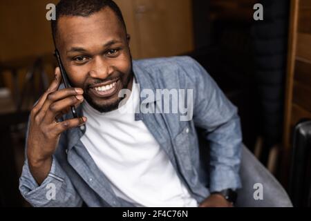 Close-up portrait of happy African American young man having fun talking on cell phone in office. Delighted with good news, has a pleasant funny Stock Photo
