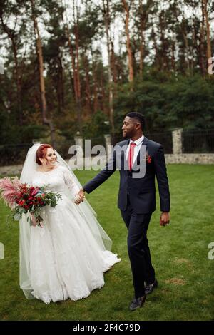 Joyful couple walking at the park, handsome African American man with lovely white woman on wedding day, beautiful bride with charming groom enjoy Stock Photo