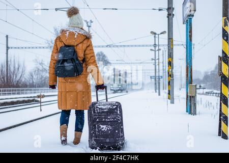Travel by train at winter. Woman standing on railroad station platform and looking at arriving train. Stock Photo