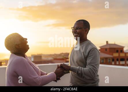 Happy Latin senior couple having romantic moment dancing on rooftop during sunset time Stock Photo