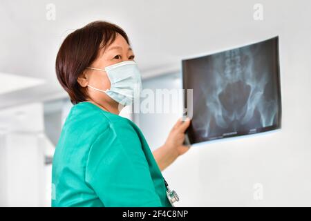Asian woman doctor with a mask looking away while holding an x-ray sheet on an out of focus background. Selective focus. Healthcare concept. Stock Photo