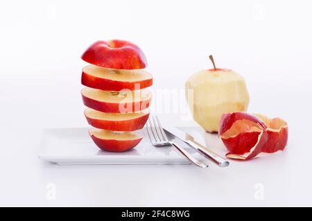 Seemingly floating red apple slices on a plate next to an apple skin and an out of focus peeled apple. Selective focus and close up. Stock Photo
