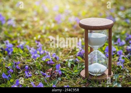Spring is here. Hourglass in flowers as a symbol of springtime. Change season. Hourglass in daylight saving time Stock Photo
