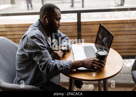 Pensive young employee businessman focused on reading news on a laptop screen, discussing a problem with a colleague in a corporate chat, checking Stock Photo