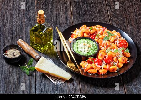 Italian potato gnocchi fried with cherry tomatoes with basil, mint and spinach pesto, parmesan cheese  - italian dish, on a black plate with golden cu Stock Photo