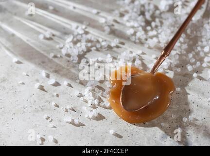 Spoon of soft homemade salted caramel on gray concrete background. Selective focus Stock Photo