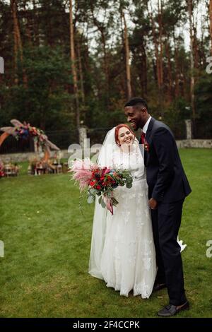 Happy couple on wedding day, smiling, handsome African American man with lovely white woman enjoy happy moment, charming groom cuddle beautiful bride Stock Photo