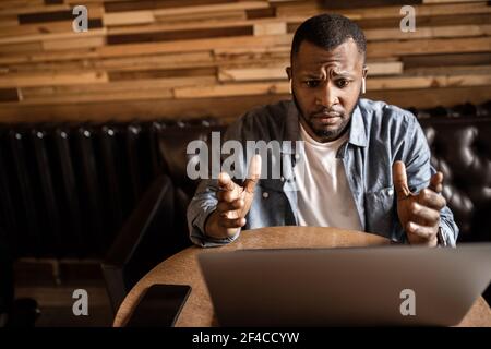 Pensive young African American businessman looking at laptop screen, discussing business plan or strategy of online project. The entrepreneur sees the Stock Photo