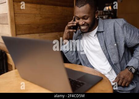 Handsome businessman is having a conversation by smartphone, smiling. Young adult male manager talking with coworkers or friends, discuss corporate Stock Photo