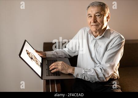 Senior joyful man sit on the sofa, looking at the camera. Happy older male having a video call with grandchildren. Caucasian grandfather use zoom Stock Photo