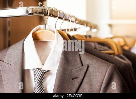 Mens suits and formal shirts with ties on wooden hangers in a clothes store Stock Photo