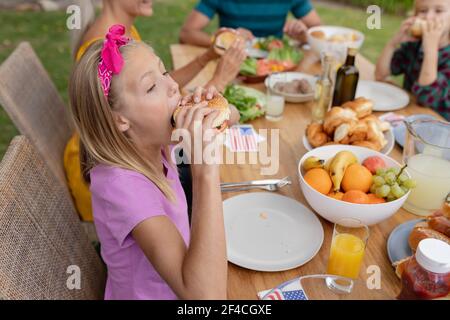 Caucasian girl eating hamburger having meal with family in garden Stock Photo