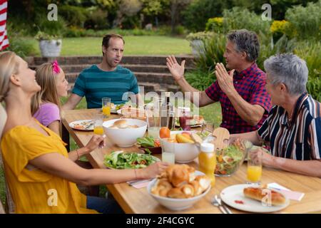 Caucasian senior man sitting at table talking with family having meal in garden Stock Photo