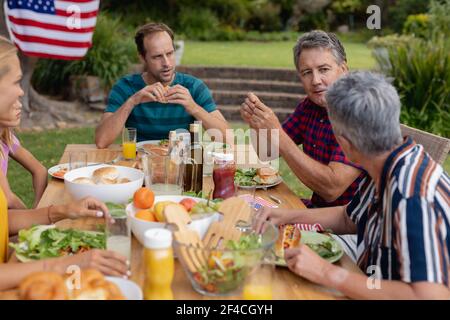 Caucasian senior man sitting at table talking with family having celebration meal in garden Stock Photo