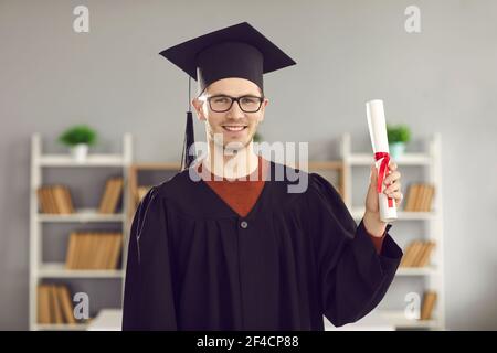 Portrait of male student in university graduate uniform showing diploma in his hands. Stock Photo