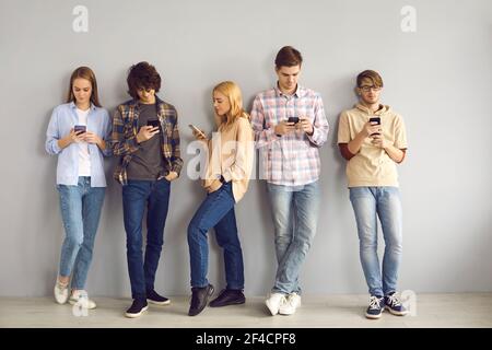 Young people leaning on wall, using mobile phones and paying no attention to each other Stock Photo