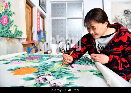 Juye, Juye County. 20th Mar, 2021. A worker draws a peony-themed realistic painting at a painting professional cooperative in Qilin Township, Juye County, Heze City of east China's Shandong Province on March 20, 2021. Heze is noted as one of the key origins of the peony flowers in China. Peony-themed, realistic-style painting as part of the traditional culture in Juye has now become an unique technique for local peasants to increase their income. Credit: Guo Xulei/Xinhua/Alamy Live News Stock Photo